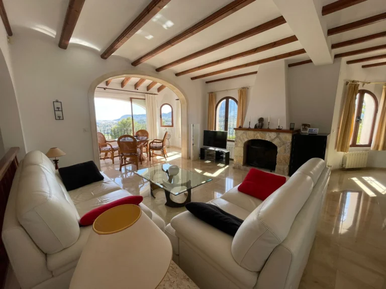 Living room with fireplace and adjoining dining area with sea views inside a villa in Calpe.