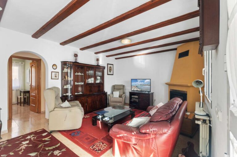Living room with fireplace and exposed ceiling beams inside a single-level villa in Calpe close to beaches and amenities.