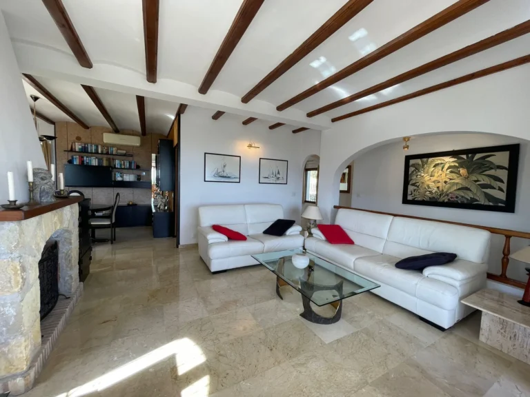 Living room with fireplace, white sofas, wood-beamed ceiling, and marble floor inside a villa in Calpe.