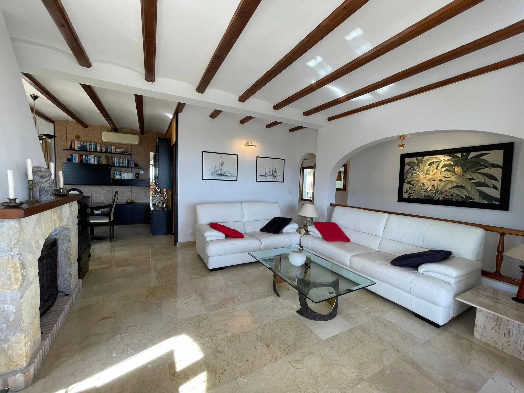 Living room with fireplace, white sofas, wood-beamed ceiling, and marble floor inside a villa in Calpe.