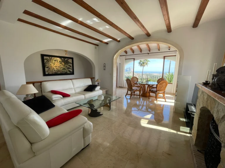 Living room with fireplace, wood-beamed ceiling, and sea views inside a villa in Calpe.