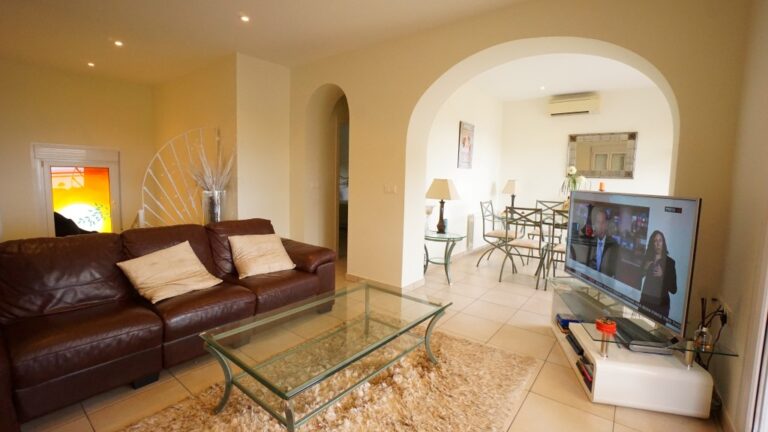 Living room with sofa, dining area, and arched opening inside a villa near La Fustera beach.