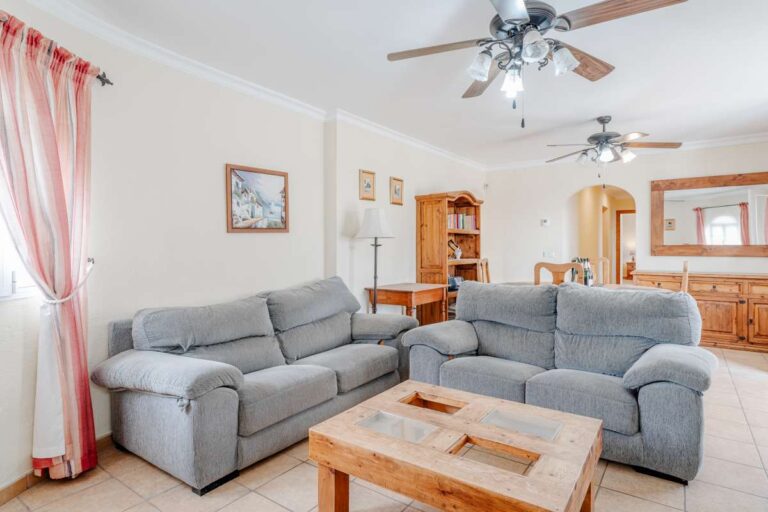 Living room with sofa seating, ceiling fans and natural light inside a Mediterranean villa with independent guest accommodation in Calpe.