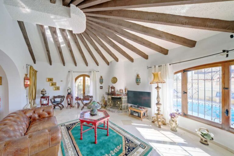 Living room with wooden beamed ceiling, fireplace and traditional details inside a second line Mediterranean villa in Calpe.