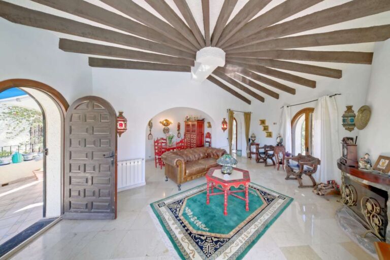 Living room with wooden beamed ceiling, traditional furniture and arched entrance inside a second line Mediterranean villa in Calpe.