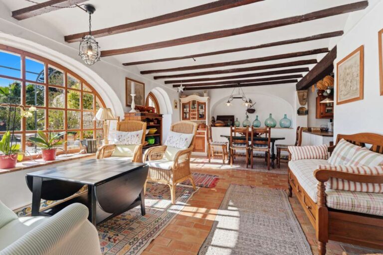Lounge and dining area inside a traditional Spanish finca near Moraira with beamed ceiling, arched window, dining table and rustic Mediterranean interior