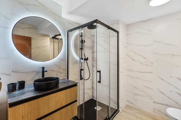 Lower level bathroom with round mirror, vanity and walk-in shower inside a modern spacious villa in Calpe.