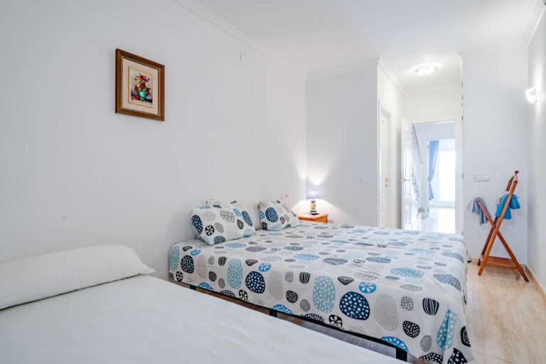 Lower-level bedroom inside a duplex apartment near Les Platgetes Beach in Moraira with double bed, bedside lighting, white walls and simple coastal interior