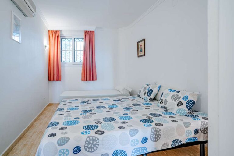Lower-level bedroom inside a duplex apartment near Les Platgetes Beach in Moraira with double bed, window, air conditioning and bright white interior