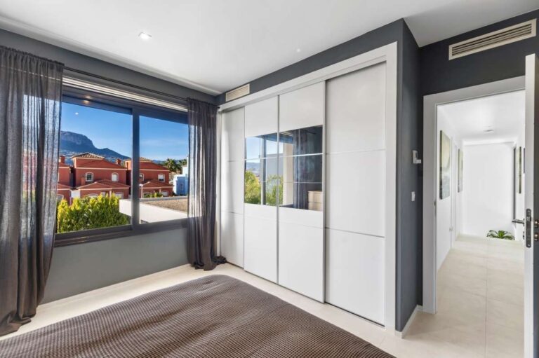 Master bedroom with fitted wardrobes, large window and natural light inside a modern oasis villa in Calpe.