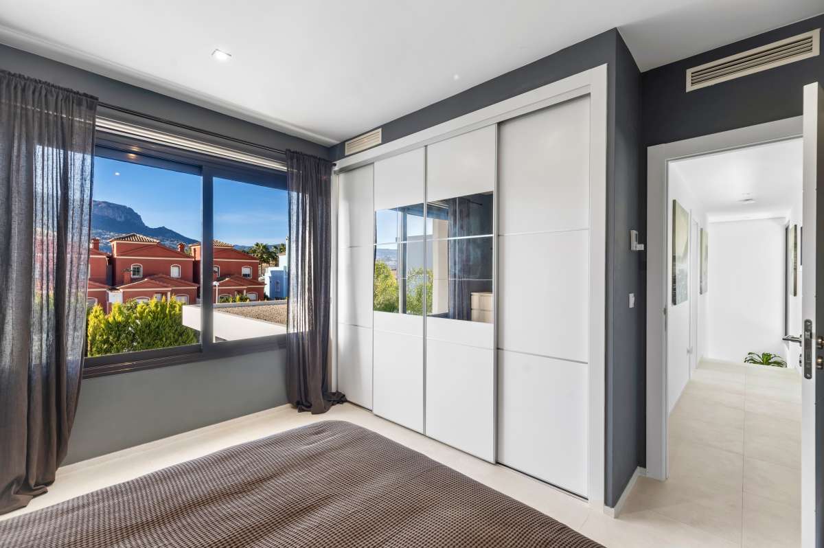 Master bedroom with fitted wardrobes, large window and natural light inside a modern oasis villa in Calpe.