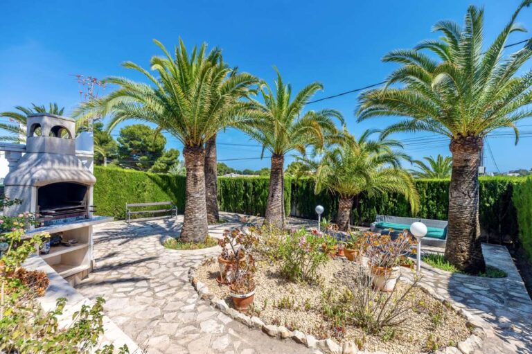 Mediterranean garden at a renovated single-level villa in Moraira with palm trees, stone paving, barbecue area and landscaped planting