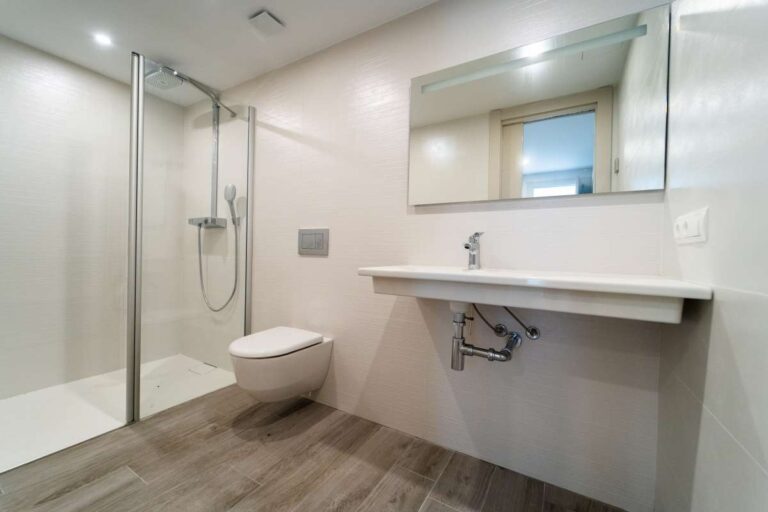 Modernes Badezimmer in einer neu gebauten Luxusvilla nahe dem Yachthafen Puerto Blanco in Calpe mit ebenerdiger Dusche, wandhängendem WC, großem Spiegel und hellen Fliesen.