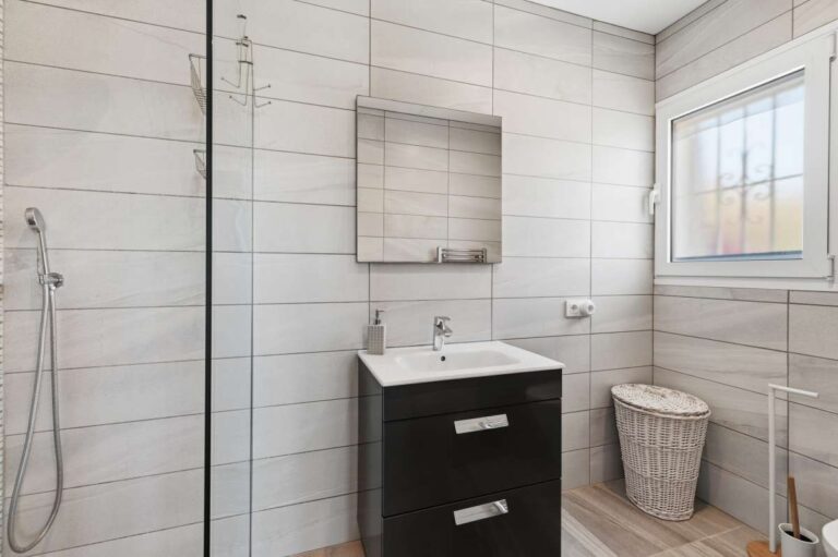 Modern bathroom inside a renovated single-level villa in Moraira with walk-in shower, vanity unit, window and bright tiled finish