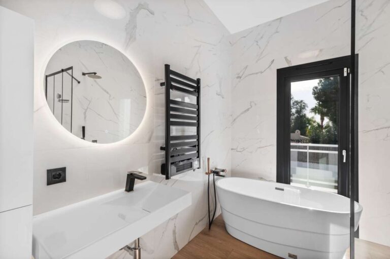 Modern bathroom inside a single-level villa in Santa Clara, Altea with bath, round mirror, black fittings, towel rail and marble-effect walls