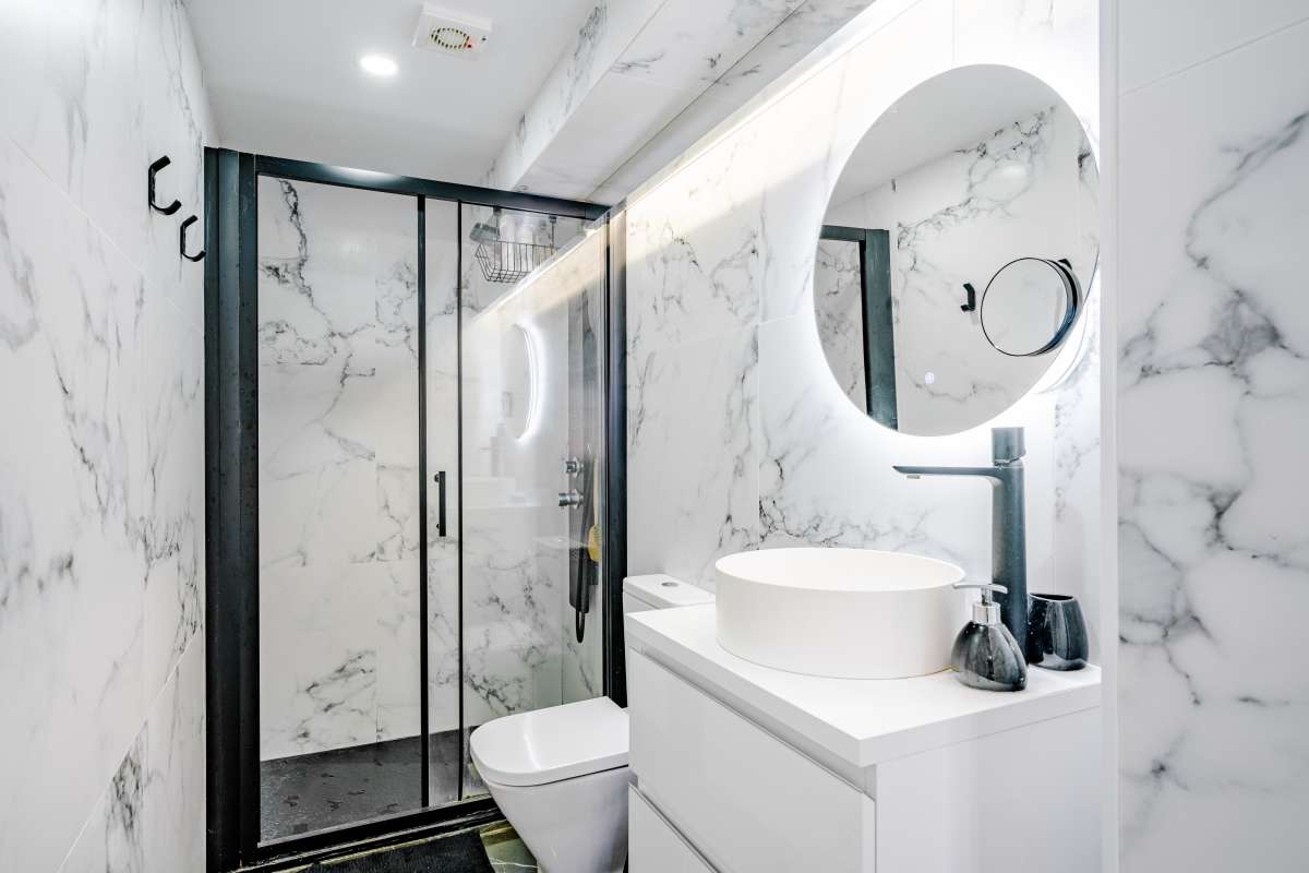 Modern bathroom with walk-in shower, round mirror and marble-effect finish inside a renovated Mediterranean villa in La Cometa, Calpe.
