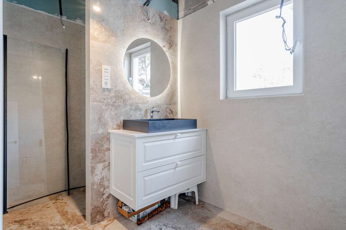 Modern bathroom with walk-in shower, vanity unit and round mirror inside a new build villa in Calpe