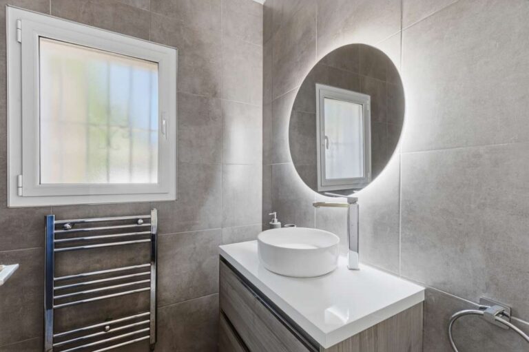 Modern en-suite bathroom inside a renovated single-level villa in Moraira with vanity unit, round mirror, towel radiator and grey tiled finish