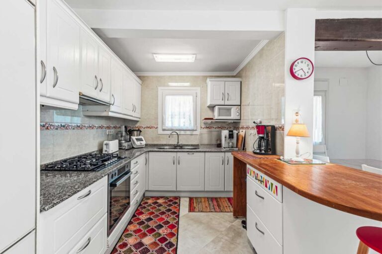 Modern fitted kitchen with white cabinets and breakfast bar inside a contemporary villa in Calpe.