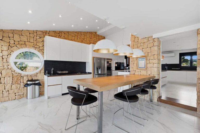 Modern kitchen and dining area inside a premium coastal villa on the Benissa Costa with stone feature wall, central dining table and integrated appliances