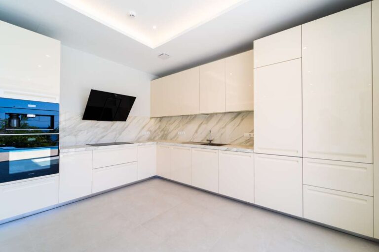 Moderne Küche in einer neu gebauten Luxusvilla in der Nähe des Yachthafens Puerto Blanco in Calpe mit weißen Schränken, integrierten Geräten und Arbeitsplatten in Marmoroptik.