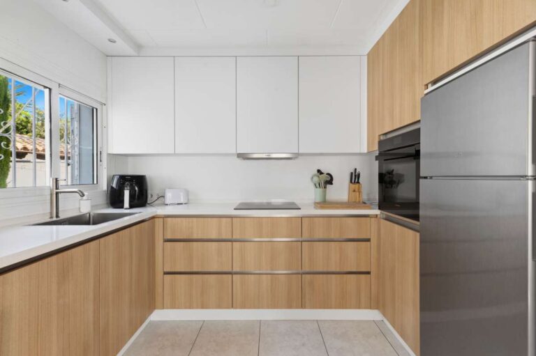 Modern kitchen inside a renovated single-level villa in Moraira with wooden cabinetry, white worktops, integrated appliances and garden views