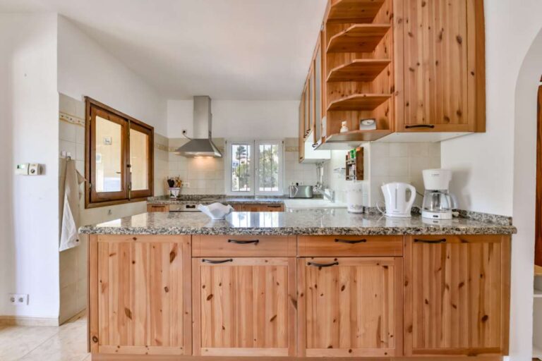 Open-plan kitchen inside a charming Benissa Coast villa with wooden cabinetry, breakfast bar, granite worktops and bright interior finish
