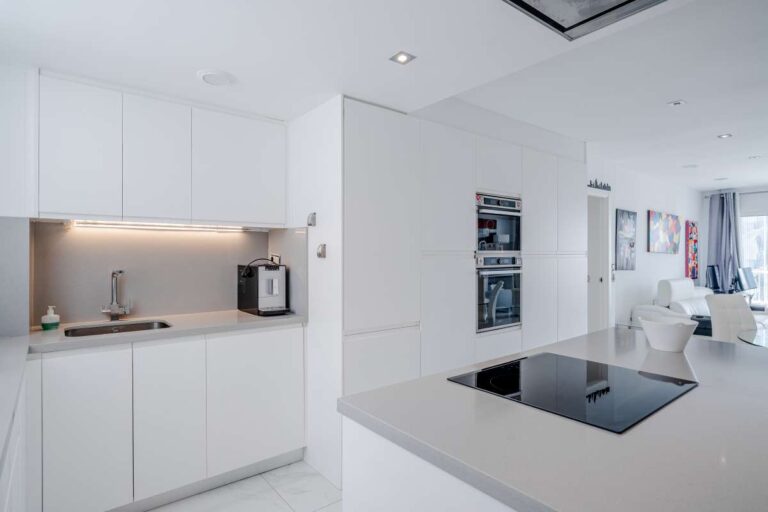 Open-plan kitchen inside a renovated apartment by Arenal-Bol Beach in Calpe with white cabinetry, kitchen island and integrated appliances