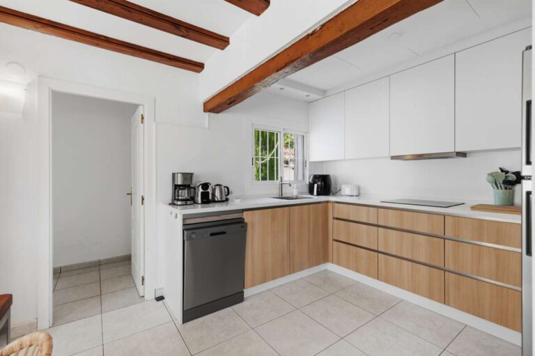 Open-plan kitchen inside a renovated single-level villa in Moraira with wooden cabinetry, white worktops, exposed beams and bright interior finish