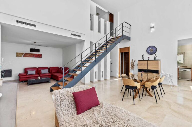Open-plan living and dining area with high ceilings and staircase inside a modern spacious villa in Calpe.