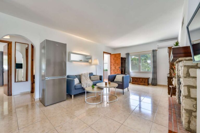 Open-plan living area inside a charming Benissa Coast villa with sofa seating, integrated kitchen, fireplace and natural light