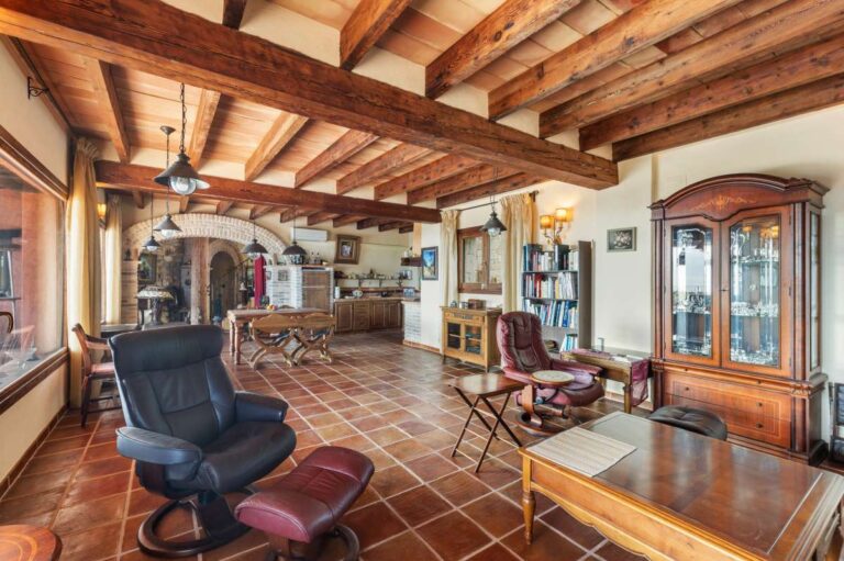 Open-plan living area inside a finca-style villa in Benissa Costa with wooden beams, rustic furniture, terracotta flooring and Mediterranean stone details