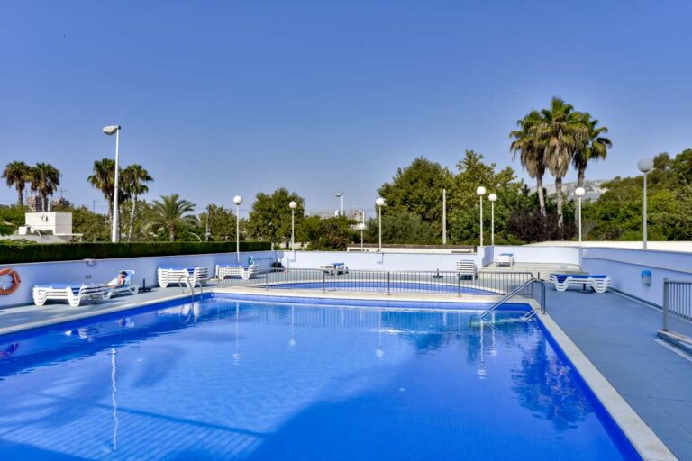 Outdoor communal swimming pool at a beachfront apartment building in La Fossa, Calpe with sun terrace and palm trees
