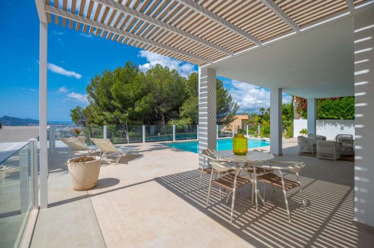 Outdoor dining terrace at a modern villa in Altea Hills with pergola, glass railing, private pool views, sea views and shaded seating area