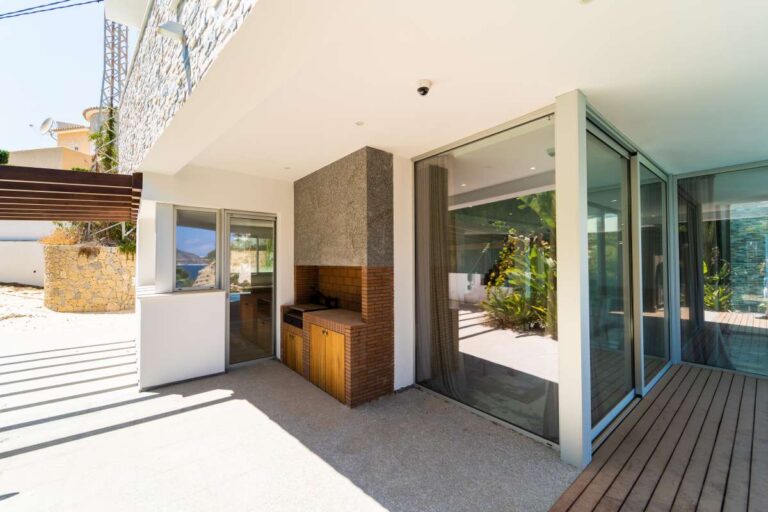 Outdoor kitchen and covered terrace at a luxury villa in Calpe with glass doors, wooden decking and poolside entertaining area