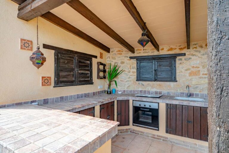 Outdoor kitchen at a historic finca in Benissa with tiled worktops, wooden cabinetry, stone walls and covered terrace area