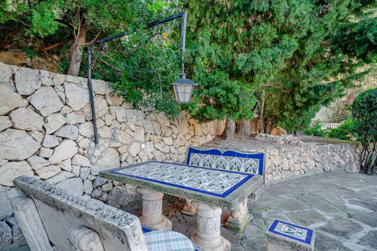 Outdoor seating area with tiled table, stone wall and Mediterranean planting at a villa in Maryvilla, Calpe.