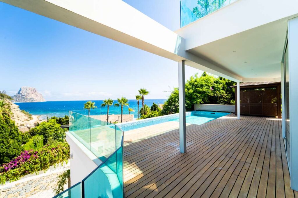 Pool terrace at a luxury villa in Calpe with panoramic sea views, glass balustrades, wooden decking and views towards the Peñón de Ifach