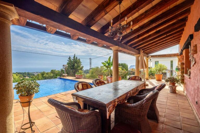Poolside dining terrace at a finca-style villa in Benissa Costa with wooden beams, outdoor dining area, infinity pool and Mediterranean Sea views