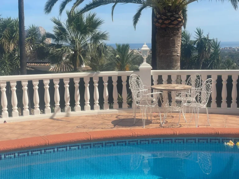 Poolside seating area with sea views, palm trees, and terrace space at a villa in Calpe.