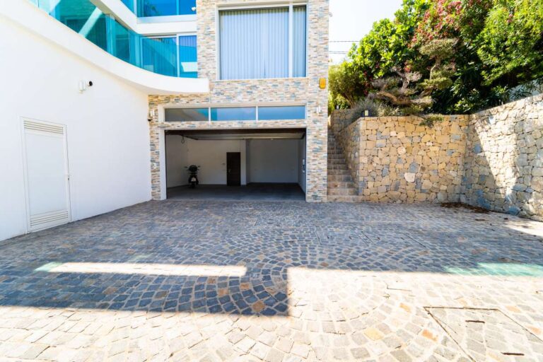 Private parking area at a luxury villa in Calpe with garage access, stone walls and spacious paved driveway