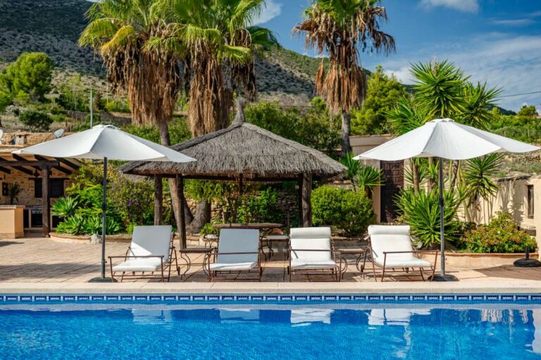 Private pool area at a historic finca in Benissa with thatched pavilion, sun loungers, parasols and Mediterranean gardens