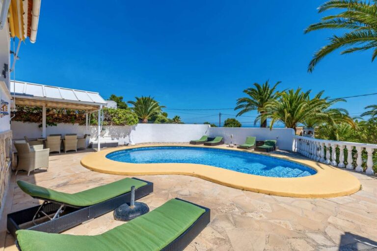 Private pool terrace at a renovated single-level villa in Moraira with sun loungers, outdoor seating, palm trees and Mediterranean garden surroundings