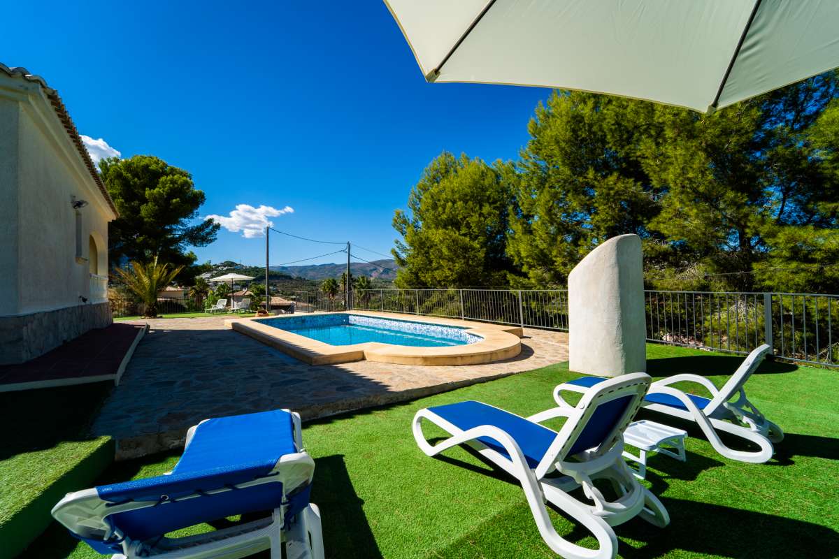Private swimming pool with sun loungers, garden area and mountain surroundings at a Mediterranean villa in Calpe.