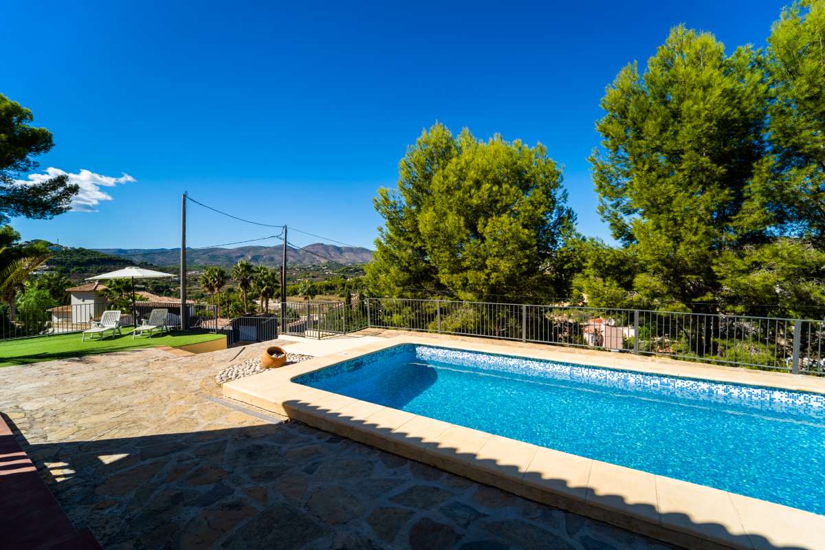 Private swimming pool with sunny terrace, trees and mountain views at a Mediterranean villa in Calpe.