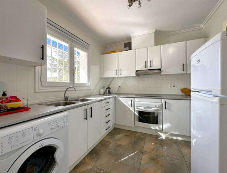 Renovated kitchen inside a single-level villa near El Portet Beach in Moraira with white cabinetry, built-in appliances, window and functional layout
