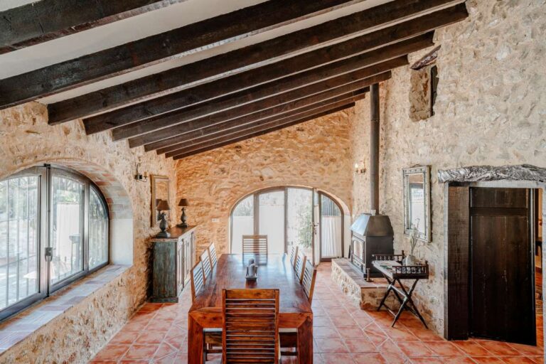 Rustic bedroom inside a historic finca in Benissa with exposed stone walls, wooden beams, arched windows and traditional tiled flooring
