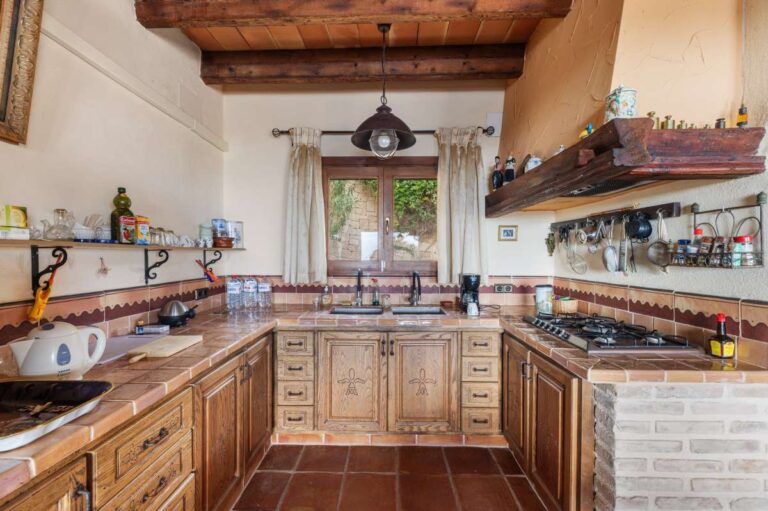 Rustic kitchen inside a finca-style villa in Benissa Costa with wooden cabinetry, tiled worktops, beamed ceiling and Mediterranean character