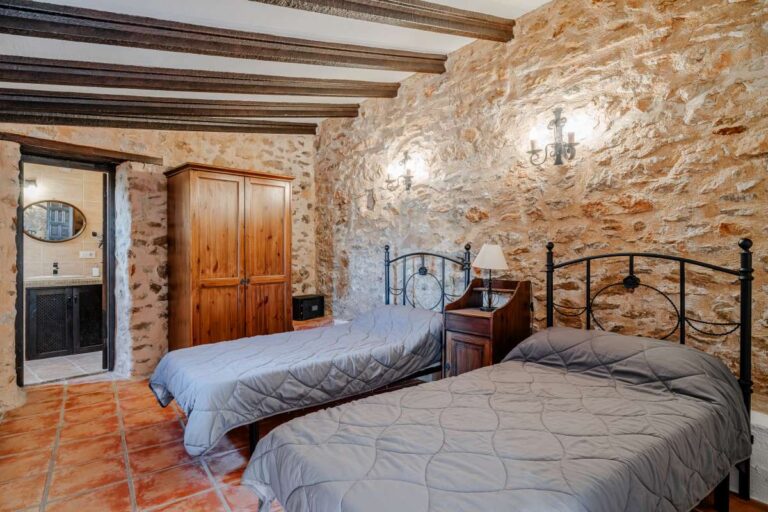 Rustic twin bedroom inside a historic luxury finca in Benissa with exposed stone walls, wooden beams and traditional Mediterranean furniture