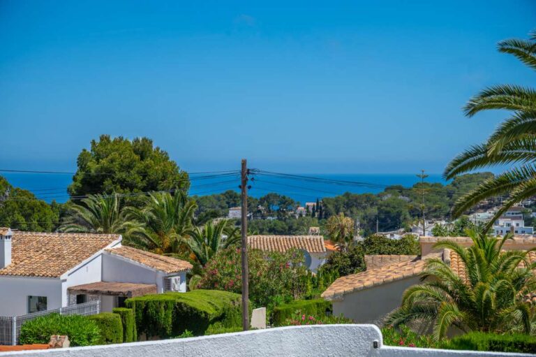 Sea views from a renovated single-level villa in Moraira with palm trees, surrounding homes and the Mediterranean coastline in the distance